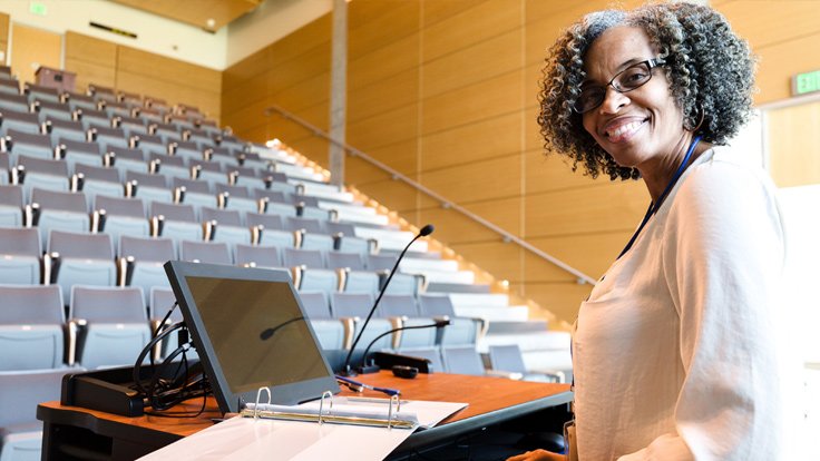 A teacher in an empty classroom holding a class online with a laptop.