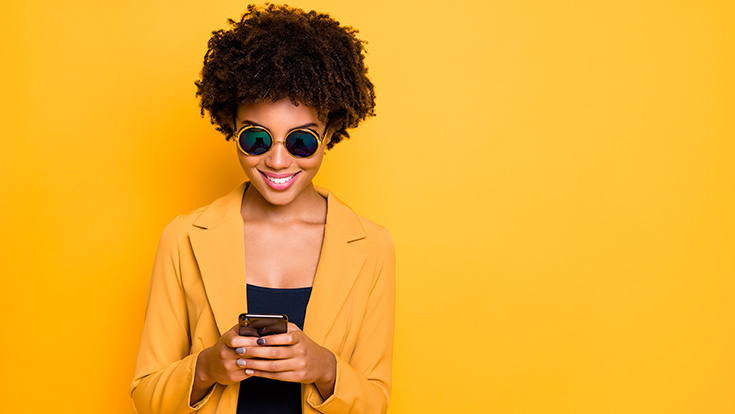 A woman using her cell phone standing against a yellow background